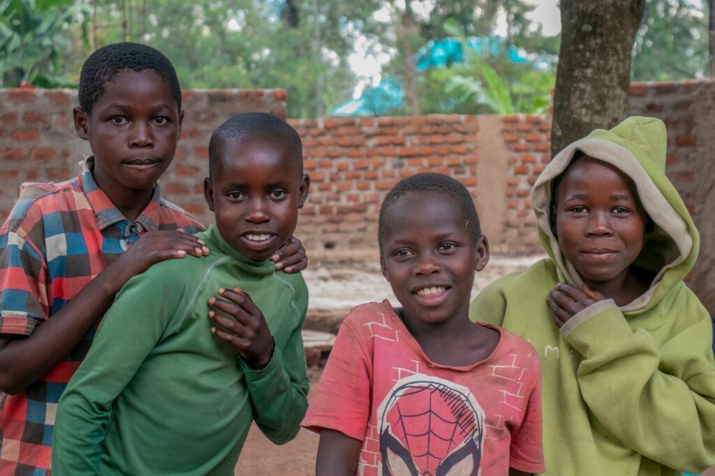 Four cheerful Ugandan children posing outdoors with smiles, showcasing friendship and joy.
