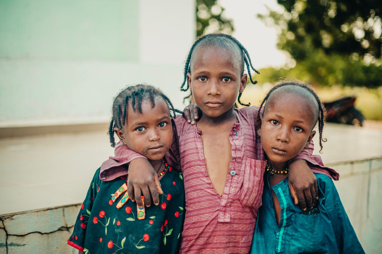 Three young children in traditional clothing standing together outdoors in Nigeria.